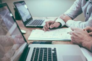 A group of real estate investors working together at a table, using laptops and tablets to analyze data and plan their investment strategies.